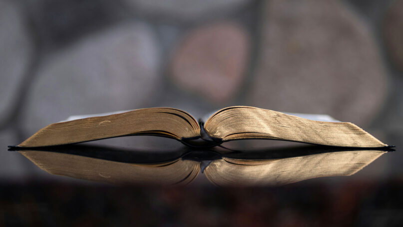 An open Bible is reflected in a table. (Photo by Aaron Burden/Unsplash/Creative Commons)